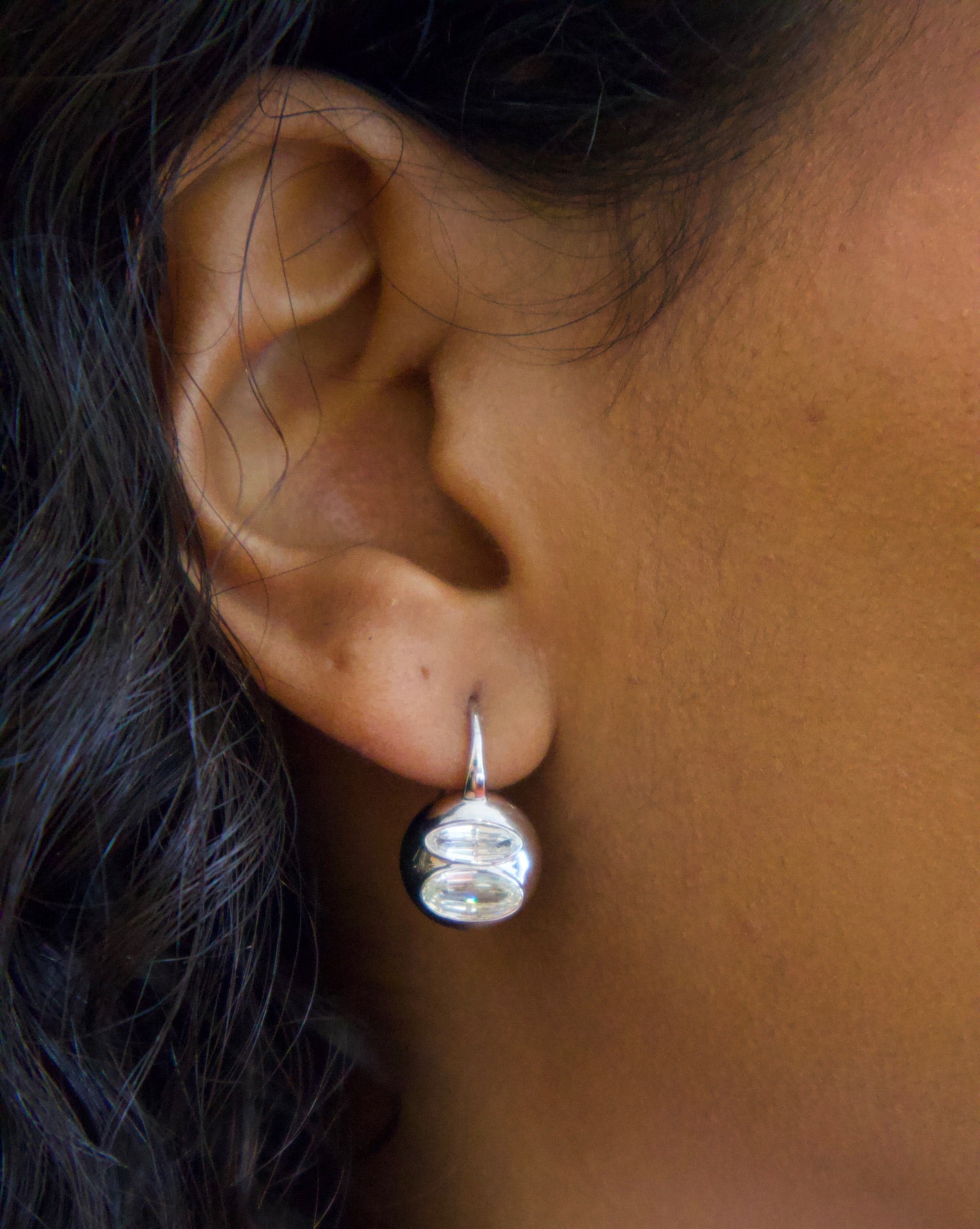 Close-up of an ear wearing a silver earring with a black background