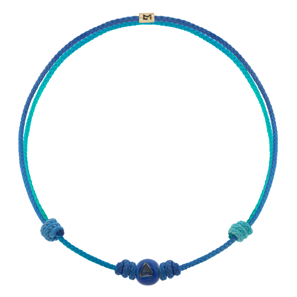 LUIS MORAIS 14K yellow gold enameled medium sized ball with a blue sapphire trillion on a cord bracelet.