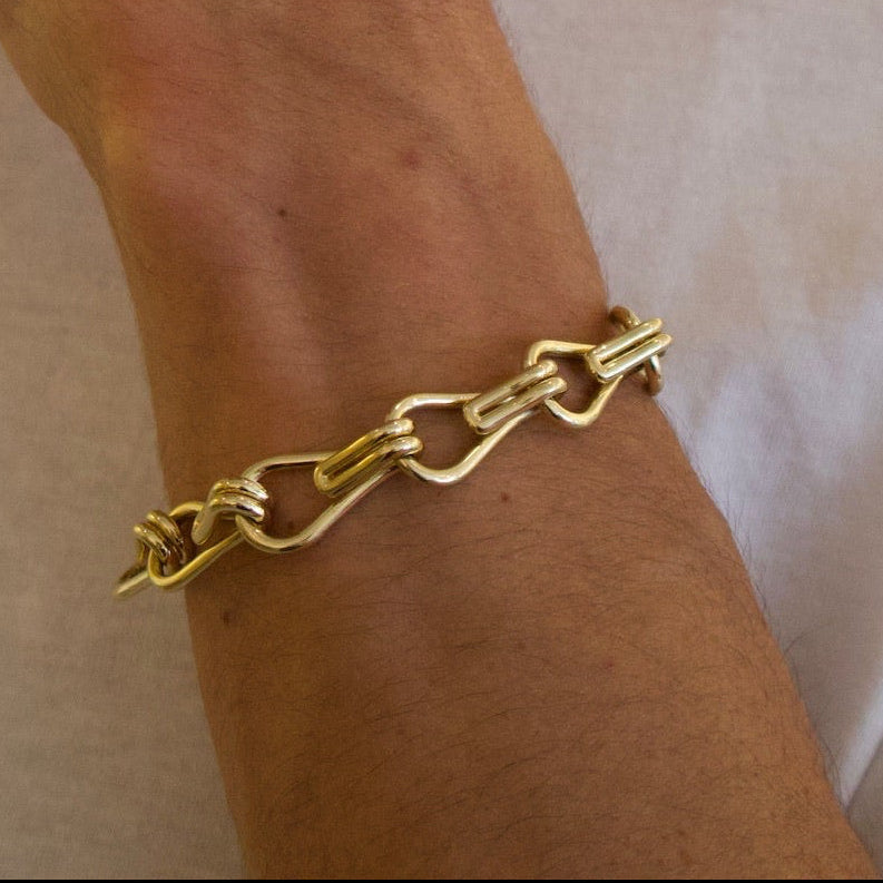 Person wearing a gold chain bracelet on a plain background