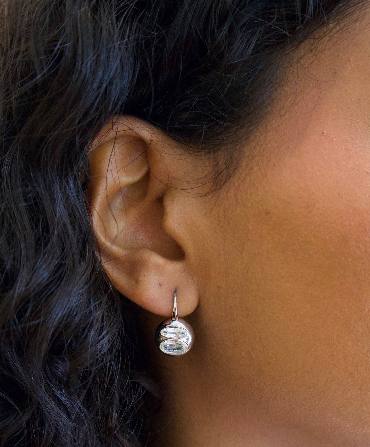 Close-up of an ear wearing a silver earring with dark hair.