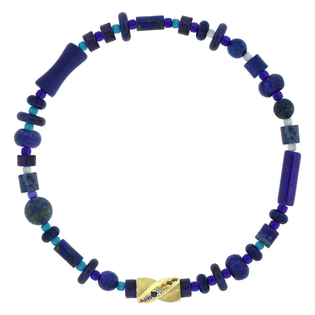 LUIS MORAIS 14k yellow gold drill bit with sapphires on a gemstone and glass beaded bracelet. The drill bit design is symbolic of digging deeper into oneself and life’s challenges. It represents resilience and the pursuit of discovery, encouraging the wearer to push through obstacles and uncover hidden truths.