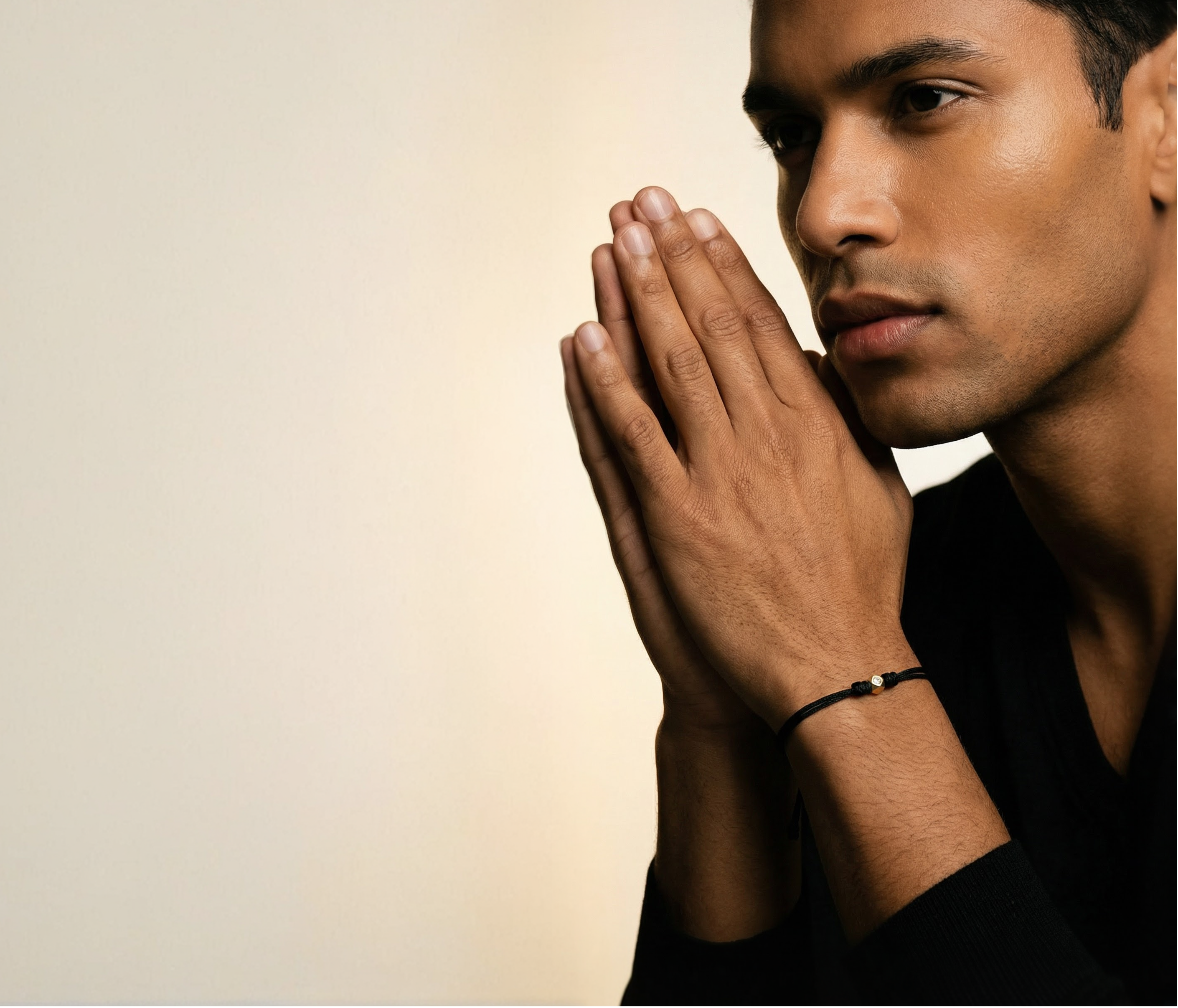 Man in a black shirt with hands pressed together against a neutral background