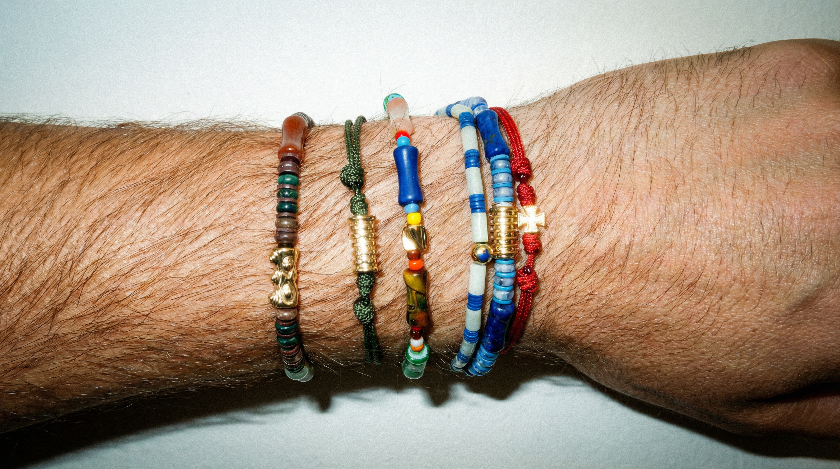 Close-up of a wrist wearing multiple colorful beaded bracelets on a plain background