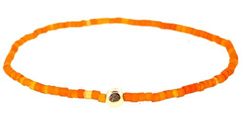 A circular glass bead bracelet with a gold ball featuring a white diamond in the center.