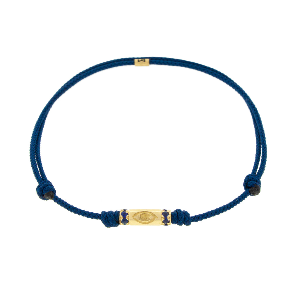 LUIS MORAIS 14K yellow gold slim tube with an evil eye symbol and two channels of blue sapphires on a navy blue cord bracelet 